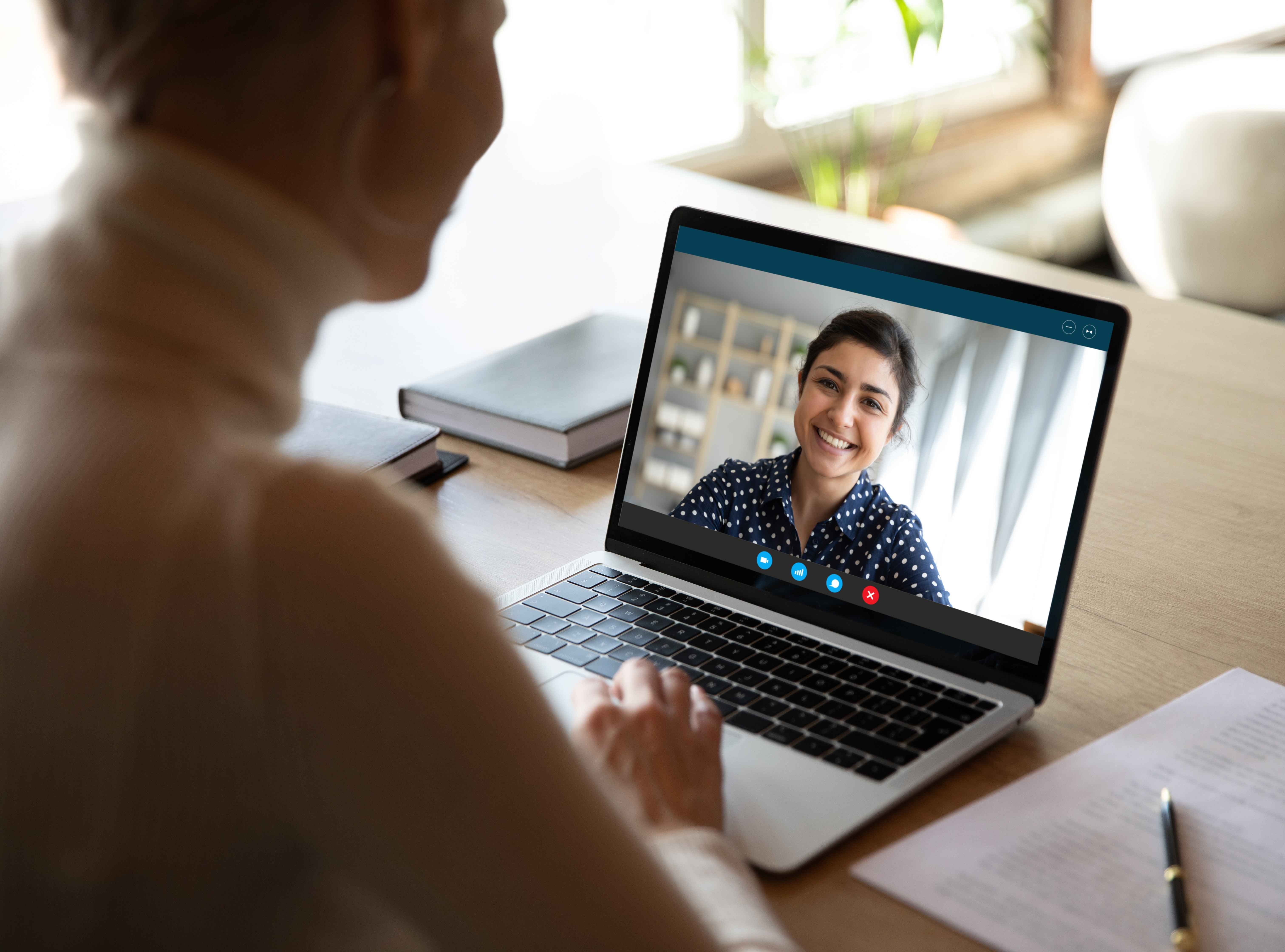 A healthcare professional on a video call with a smiling colleague on a laptop screen